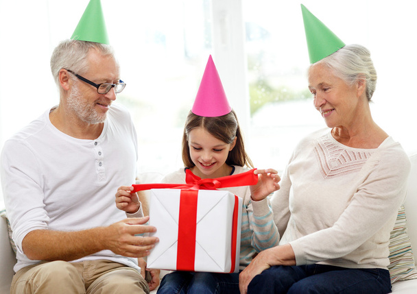 Lächelnde Familie in Party-Hüten mit Geschenkbox zu Hause - Foto, Bild