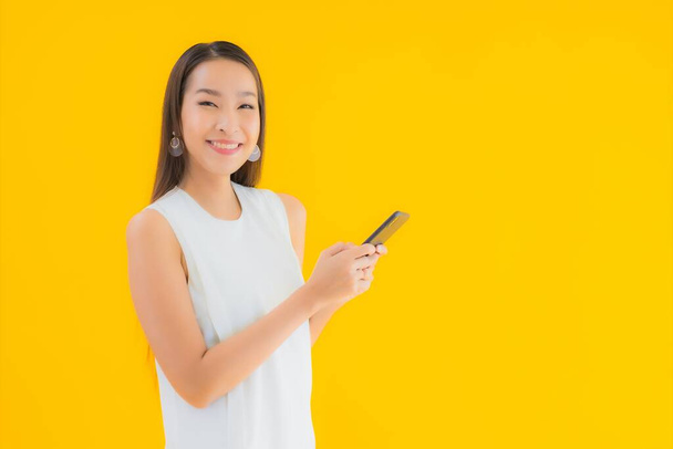 Retrato hermosa joven asiática mujer con teléfono móvil inteligente en amarillo aislado fondo - Foto, imagen