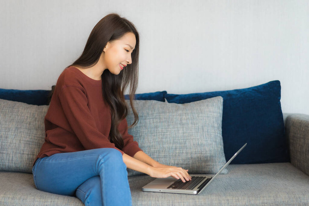 Portret piękna młoda azjatycka kobieta używać laptopa na kanapie w salonie wnętrze - Zdjęcie, obraz