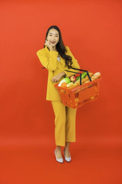 Portret mooie jonge aziatische vrouw met boodschappenmand van supermarkt op rode achtergrond - Foto, afbeelding