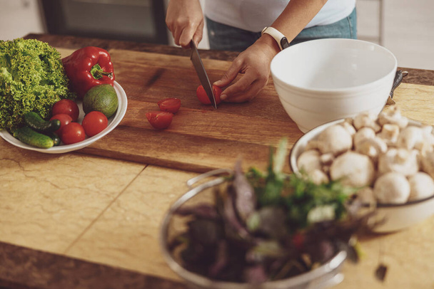 Zubereitung eines Salats aus Tomaten, Gurken, Pilzen und Basilikum in der Küche - Foto, Bild