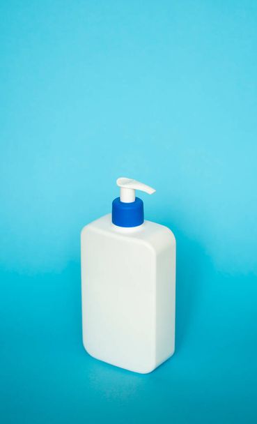 Large white plastic bottle with pump dispenser as a liquid container for gel, lotion, cream, shampoo, bath foam on blue background - Фото, зображення