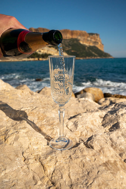 Despejando de vinho espumante de champanhe francês em vidro e vista para a praia, água do mar azul e montanhas em Cassis, Provence, França - Foto, Imagem