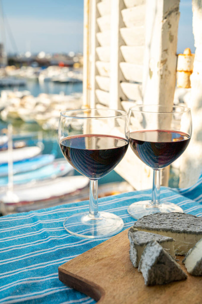 Sommerfest mit provenzalischem Rotwein und Käse auf der Außenterrasse mit Blick auf den alten Fischerhafen mit bunten Booten in Cassis, Provence, Frankreich - Foto, Bild