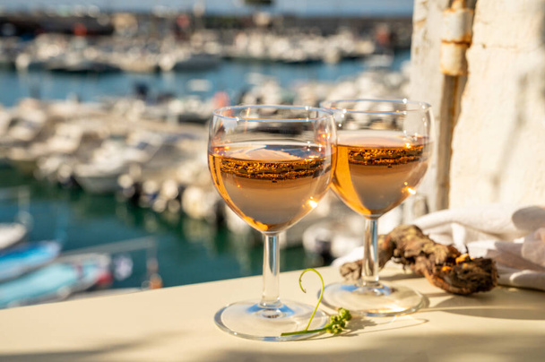 Summer party with cold rose Provencal wine in glass served in sunlights on outdoor terrace with view on old fisherman's harbour with colourful boats in Cassis, Provence, France - Photo, Image