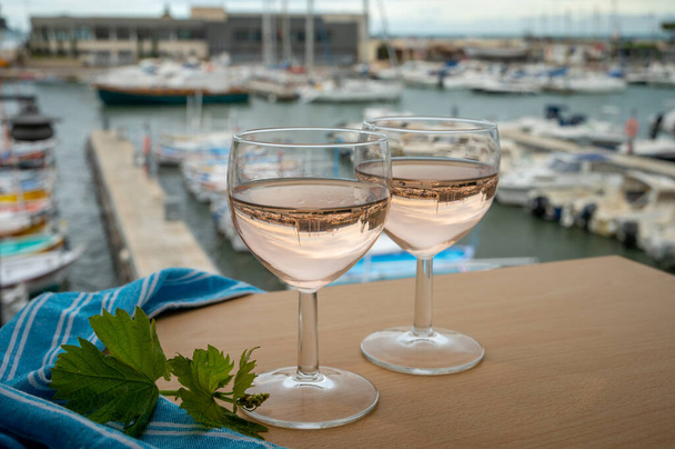 Vino provenzal rosa en copas servido en la terraza al aire libre con vistas al puerto de pescadores de edad con coloridos barcos en Cassis, Provenza, Francia - Foto, Imagen