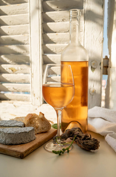 Chladná růže Provencal víno ve skle a láhvi podávané s kozím sýrem na venkovní terase s výhledem na starý rybářský přístav s barevnými čluny v Cassis, Provence, Francie - Fotografie, Obrázek