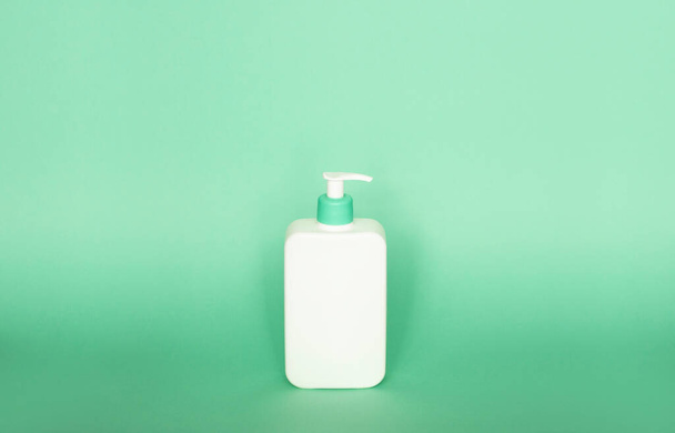 Large white plastic bottle with pump dispenser as a liquid container for gel, lotion, cream, shampoo, bath foam on green background - Fotoğraf, Görsel