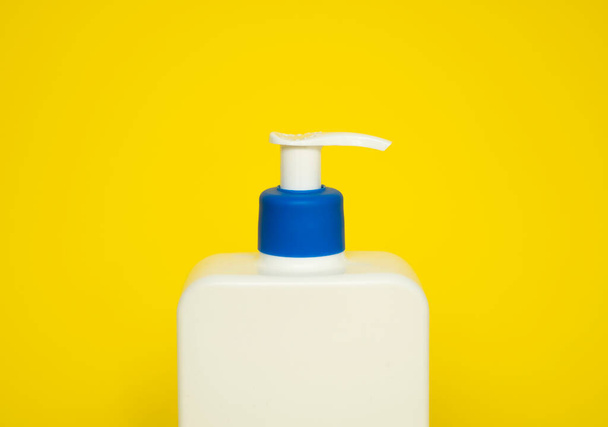 Large white plastic bottle with pump dispenser as a liquid container for gel, lotion, cream, shampoo, bath foam on yellow background - Fotó, kép