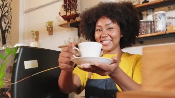 Afro-Amerikaanse vrouwelijke barista in kijkt naar camera, biedt kopje koffie aan de klant met een vrolijke glimlach, happy service werkt in casual restaurant cafe, jonge kleine onderneming startup ondernemer. - Video