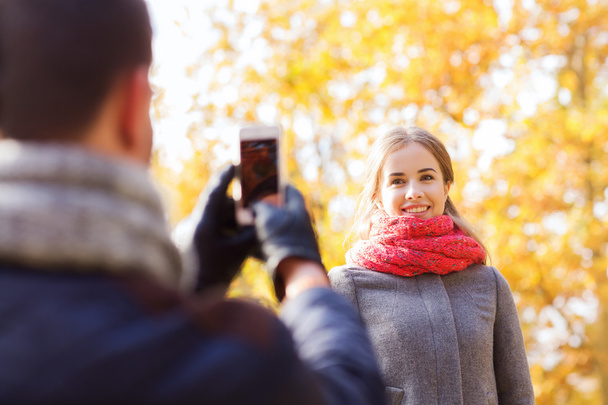 smiling couple with smartphone in autumn park - Zdjęcie, obraz