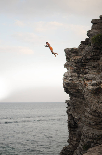 A man is jumping from a high cliff into the sea on a sunny day - Fotoğraf, Görsel