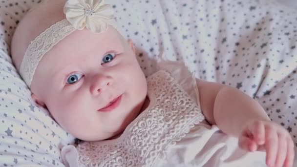Feche a linda menina com yeas azuis jaz na cama e sorri para a câmera. Desenvolvimento infantil no primeiro ano de vida. Protecção das crianças, adopção, conceito de maternidade - Filmagem, Vídeo