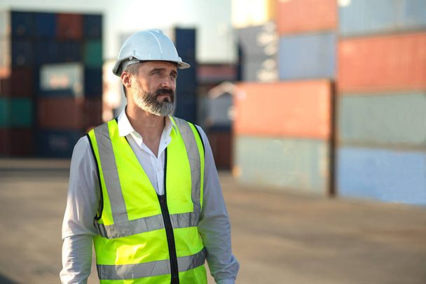 Caucasian male manager in white hard hat helmet and high-visibility vest walking in Container Terminal. - Foto, immagini