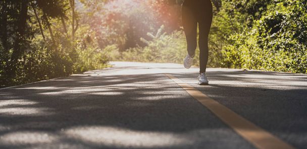 女性が公園の道路をジョギングしている、彼女は多くの人が朝と夕方のジョギングに来る公園で実行されている、実行している人気のアクティビティです。ジョギングと健康管理の概念. - 写真・画像