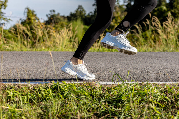 Eine Frau joggt auf einer Parkstraße, sie läuft in einem Park, wo viele Leute morgens und abends zum Joggen kommen, Laufen ist eine beliebte Aktivität. Gesundheitskonzept mit Joggen. - Foto, Bild