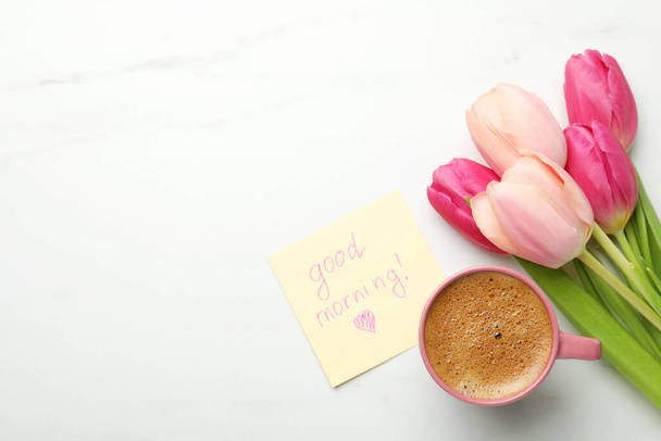 Cup of aromatic coffee, beautiful pink tulips and Good Morning note on white marble table, flat lay. Space for text - Fotografie, Obrázek