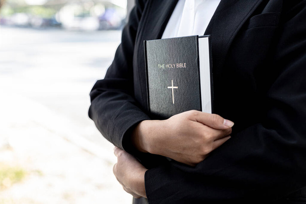A person is holding a Bible book, he is praying to the Bible, he is reading and studying the Bible. Concept of Christianity and Bible Study. - Photo, Image