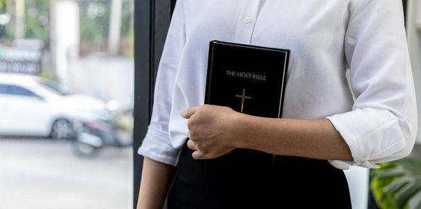 A person is holding a Bible book, he is praying to the Bible, he is reading and studying the Bible. Concept of Christianity and Bible Study. - Photo, Image