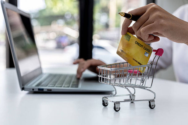 Kredi kartı tutan ve dizüstü bilgisayarda yazan bir kadın, bir İnternet alışveriş sitesinde sipariş verebilmek için kredi kartı bilgilerini dolduruyor. Çevrimiçi alışveriş ve kredi kartı ödeme kavramı - Fotoğraf, Görsel