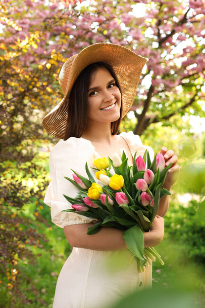 Beautiful young woman with bouquet of tulips in park on sunny day - Fotó, kép
