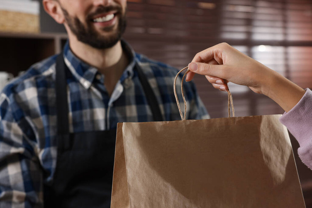 Worker giving paper bag to customer in cafe, closeup - Fotó, kép
