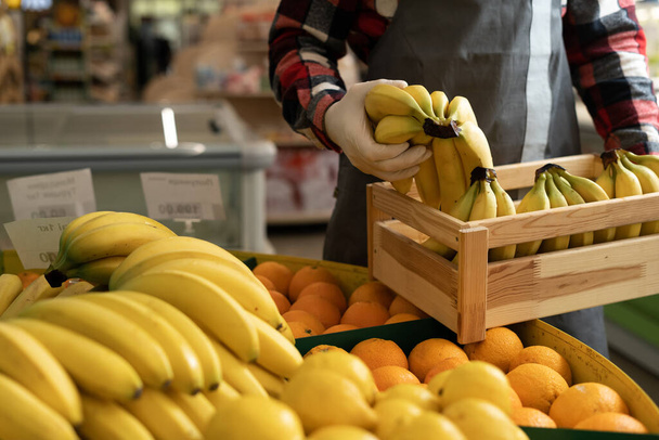 hands of a supermarket seller worker in an apron arranging citrus fruits and bananas in the fruit section, close-up - Valokuva, kuva