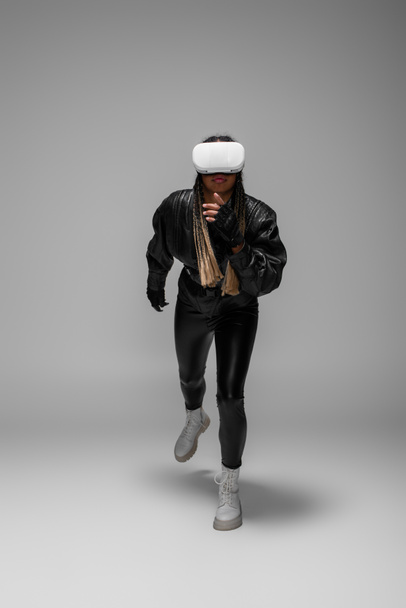 Volle Länge der afrikanisch-amerikanischen Frau in vr Headset läuft auf grauem Hintergrund  - Foto, Bild