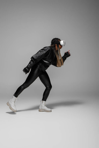 Side view of african american woman in vr headset running on grey background  - Zdjęcie, obraz
