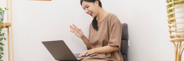 Rahatlama yaşam tarzı konsepti. Genç Asyalı kadın, arkadaşıyla oturma odasında video görüşmesi yapmak için dizüstü bilgisayar kullanıyor.. - Fotoğraf, Görsel