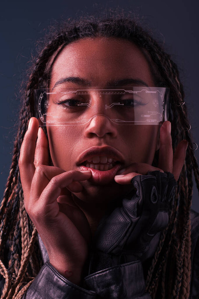Portrait of african american woman in glove and smart glasses looking at camera isolated on dark grey  - Valokuva, kuva
