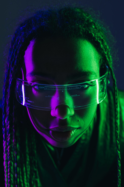 Retrato de mujer afroamericana con coletas usando gafas inteligentes aisladas en azul oscuro  - Foto, Imagen