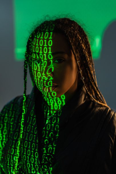 Африканська американка з проекцією комп "ютерного коду дивиться на камеру на сірому фоні.  - Фото, зображення