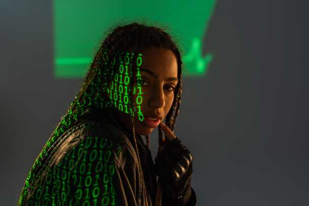 Afroamerikanerin in Lederjacke mit Computercode-Projektion auf grauem Hintergrund  - Foto, Bild