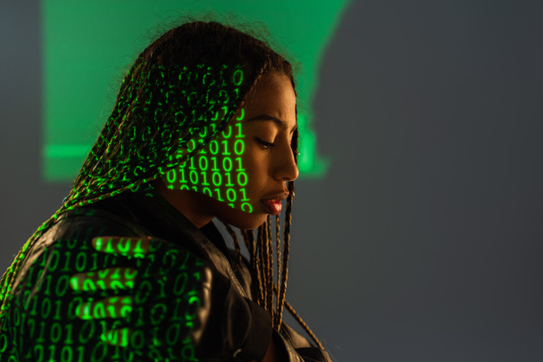 Vista lateral de mujer afroamericana con proyección de código binario sobre fondo gris  - Foto, imagen