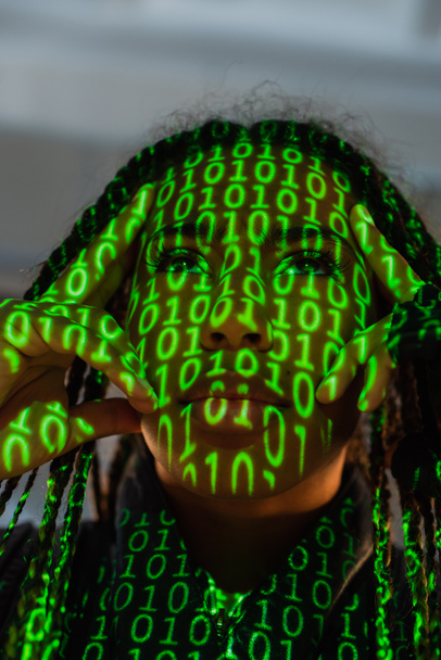 Χαμηλή γωνία άποψη της αφρικανικής αμερικανικής γυναίκας με προβολή του κώδικα του υπολογιστή σε γκρι φόντο  - Φωτογραφία, εικόνα
