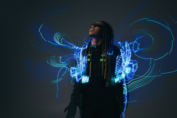 Stylish african american woman in smart glasses standing near abstract projection on grey background  - Foto, immagini