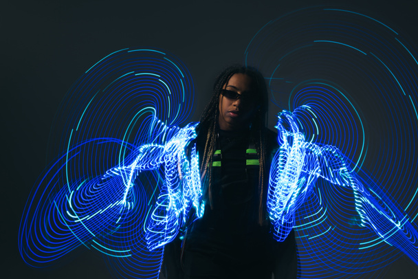 African american woman in smart glasses standing near neon lights on grey background  - Fotó, kép