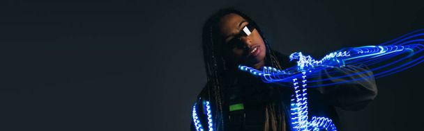 African american woman in smart glasses standing near neon lights on grey background, banner  - Foto, imagen
