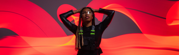 African american woman in smart glasses standing on red abstracted background, banner  - 写真・画像
