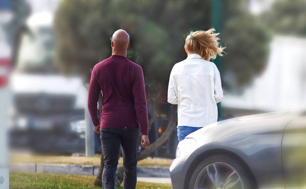 A bald man with a blonde walking through a parking lot - Photo, Image