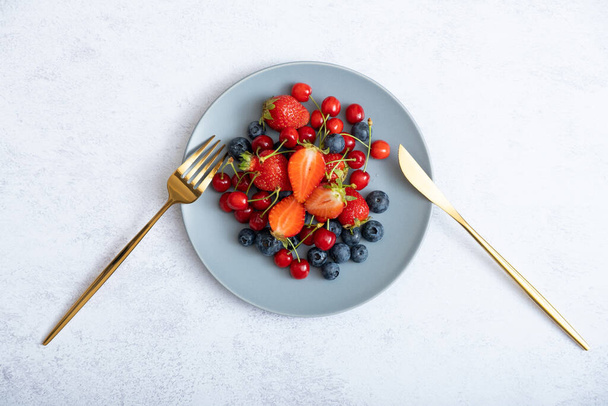Strawberries, cherries and blueberries on a plate with a knife and fork, top view. - Foto, afbeelding