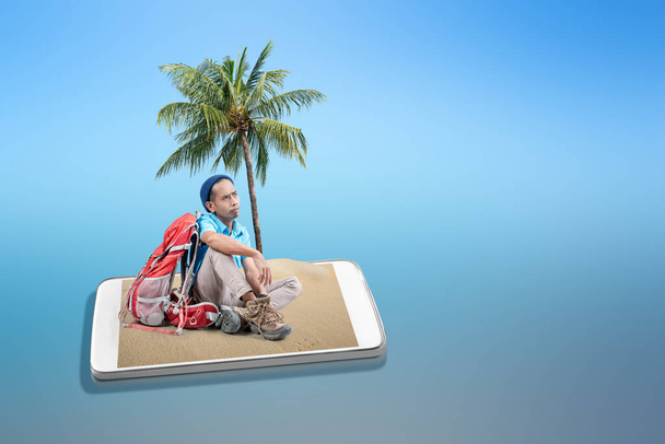 Mobile phone screen with sandy beach. Asian man with a beanie hat sitting with his backpack on the sandy beach on the mobile phone screen. Traveling concept - Foto, Bild