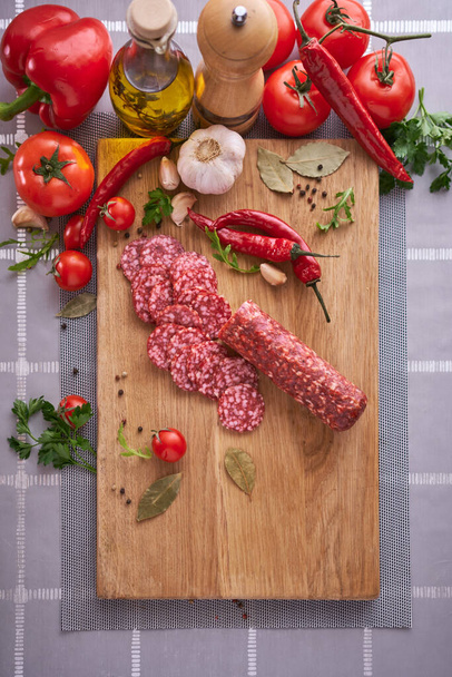 Sliced salami sausage on wooden cutting board at domestic kitchen. - Fotoğraf, Görsel