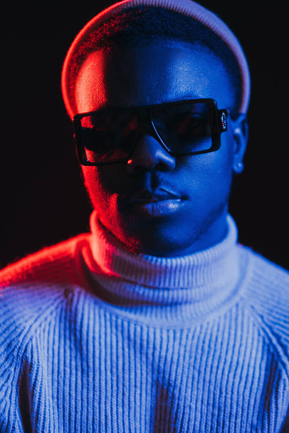 Neon light man. Night portrait. Cyberpunk fashion. Cool handsome guy face in sunglasses in bright red blue glow isolated on dark background. - Fotografie, Obrázek