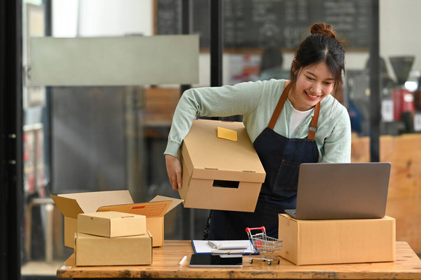 Kisvállalkozás tulajdonosa kötény segítségével laptop, miközben dolgozik a raktárban az online eladó. - Fotó, kép