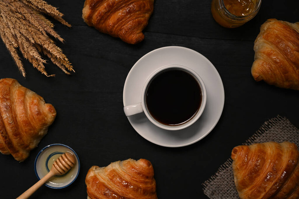 Xícara de café e croissants recém-assados na mesa de madeira preta. Vista superior. - Foto, Imagem