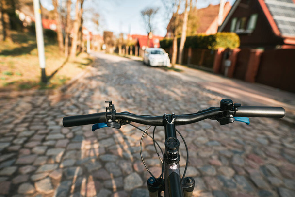 Άποψη πρώτου προσώπου του χειρισμού του ποδηλάτου στον άδειο ασφαλτοστρωμένο δρόμο της πόλης προς το φως του ήλιου. Έννοια της χρήσης ποδηλάτου για μετακίνηση στην πόλη. - Φωτογραφία, εικόνα