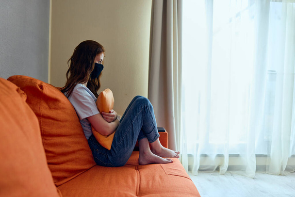 hermosa mujer con una máscara se sienta en un sofá naranja en el estilo de vida de casa. Foto de alta calidad - Foto, Imagen