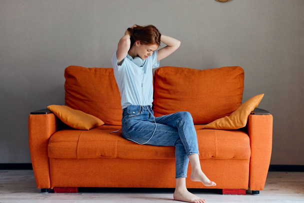 iloinen nainen kuuntelee musiikkia kuulokkeet oranssi sohva elämäntapa. Laadukas kuva - Valokuva, kuva